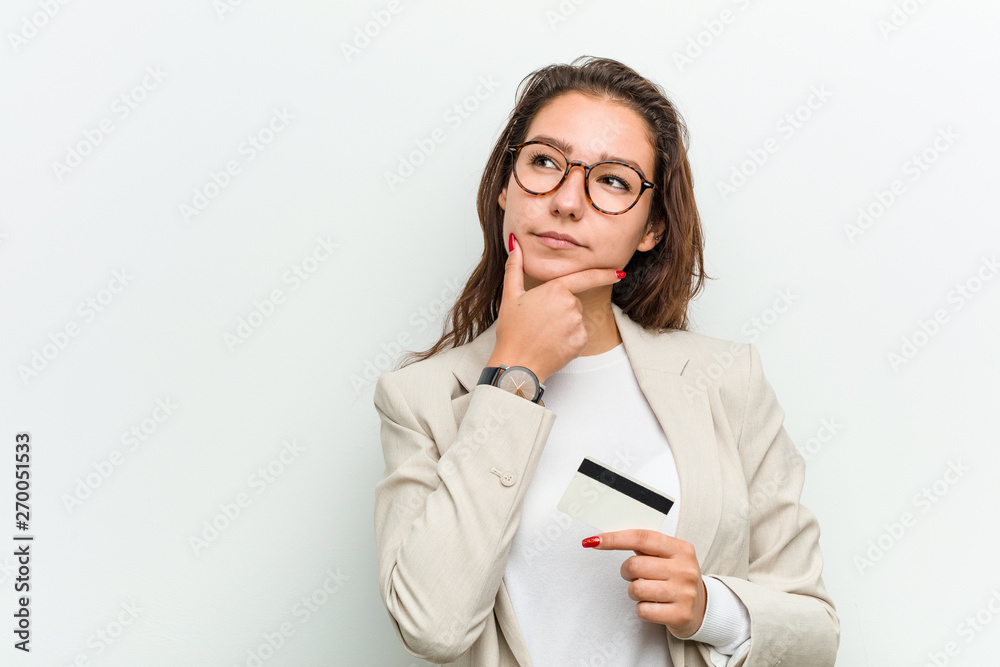 Young european business woman holding a credit card looking sideways with doubtful and skeptical expression. Young european business woman holding a credit card looking sideways with doubtful and skeptical expression.