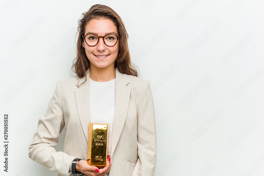 Young european business woman holding a gold ingot happy, smiling and cheerful. Young european business woman holding a gold ingot happy, smiling and cheerful.