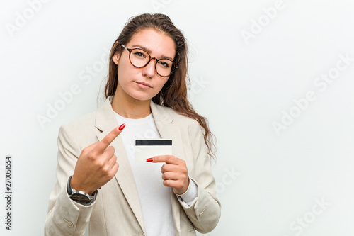 Young european business woman holding a credit card pointing with finger at you as if inviting come closer.