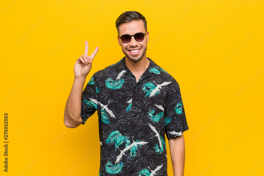 Young filipino man wearing summer clothes joyful and carefree showing a peace symbol with fingers.