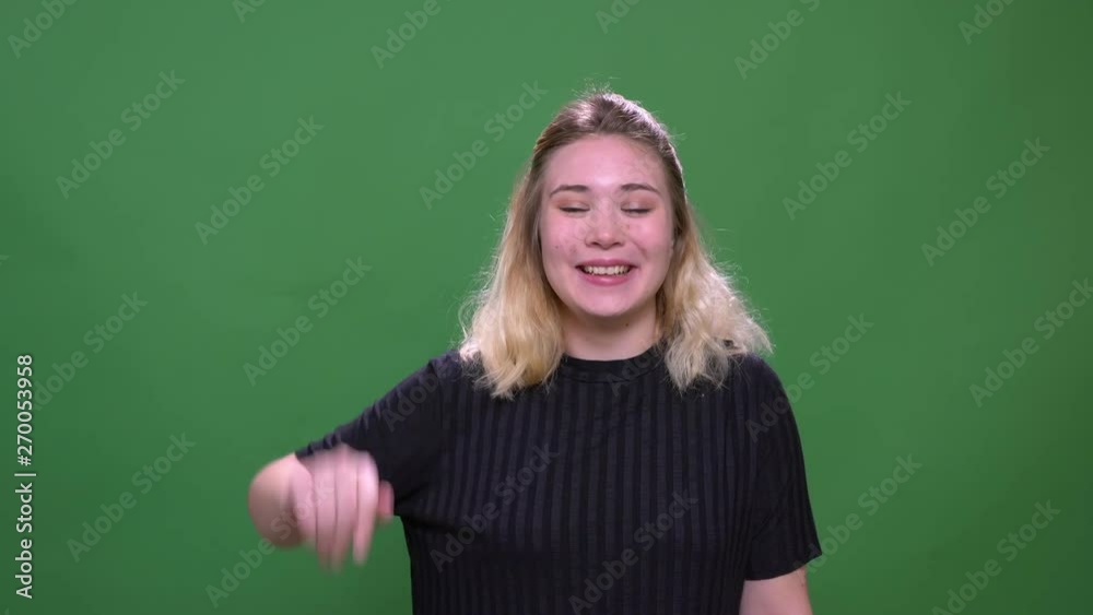 Closeup portrait of young pretty blonde caucasian female waving hi smiling with excitement looking at camera with background isolated on green Closeup portrait of young pretty blonde caucasian female waving hi smiling with excitement looking at camera with background isolated on green