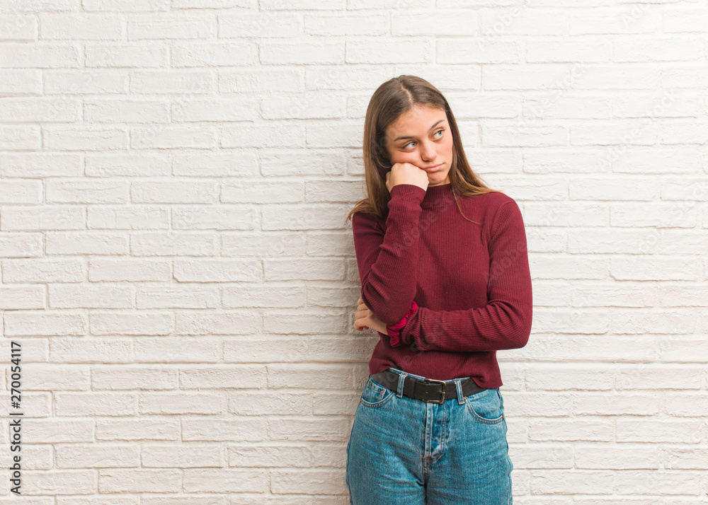 Young cool woman over a bricks wall thinking of something, looking to the side Young cool woman over a bricks wall thinking of something, looking to the side