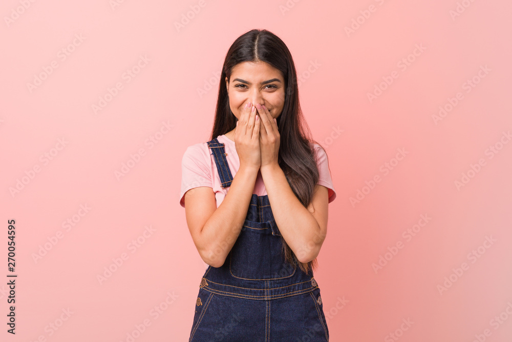 Young pretty arab woman wearing a jeans dungaree laughing about something, covering mouth with hands. Young pretty arab woman wearing a jeans dungaree laughing about something, covering mouth with hands.
