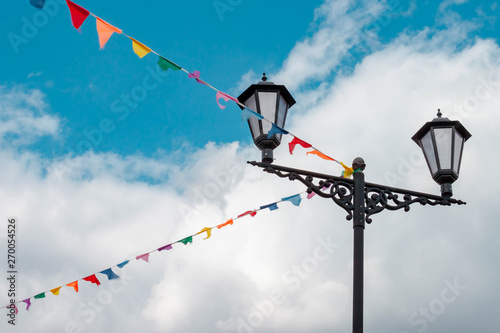 festive colorful triangle flags hanging on ropes on blue sky and white clouds background.