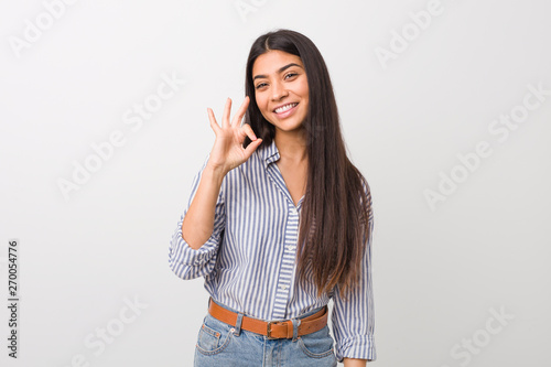 Young pretty arab woman winks an eye and holds an okay gesture with hand.