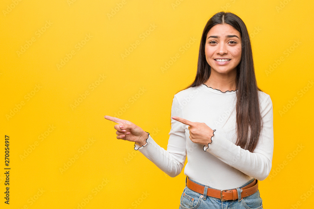 Young pretty arab woman against a yellow background shocked pointing with index fingers to a copy space. Young pretty arab woman against a yellow background shocked pointing with index fingers to a copy space.