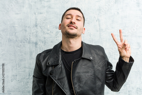 Young rocker man joyful and carefree showing a peace symbol with fingers.