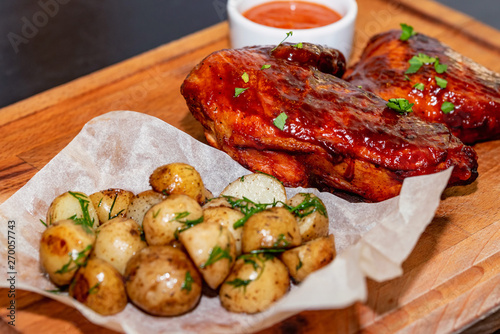 Smoked chicken thights served with potato and sauce on wooden tray close photo