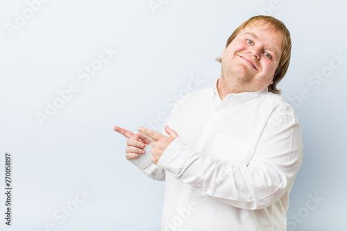 Young authentic redhead fat man excited pointing with forefingers away.