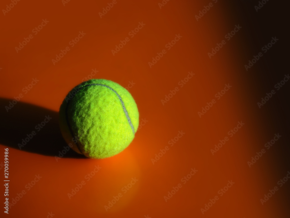 Closeup of a green tennis ball on an orange background with strong shadow casting to the left side.