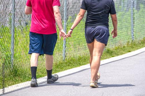 Cropped picture of two young adults wearing shorts and tee shirts on paved walking trail with fingers intertwined - cropped and unrecognizable - selective focus