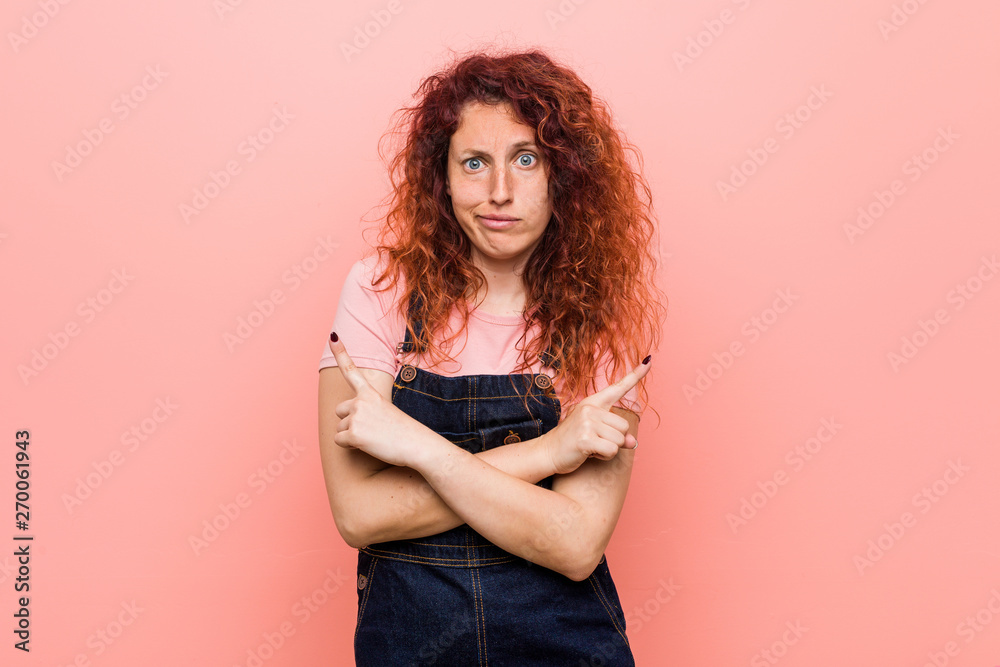 Young pretty ginger redhead woman wearing a jeans dungaree points sideways, is trying to choose between two options. Young pretty ginger redhead woman wearing a jeans dungaree points sideways, is trying to choose between two options.