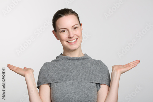 young smiling woman in grey sweater makes a not know gesture with her arms