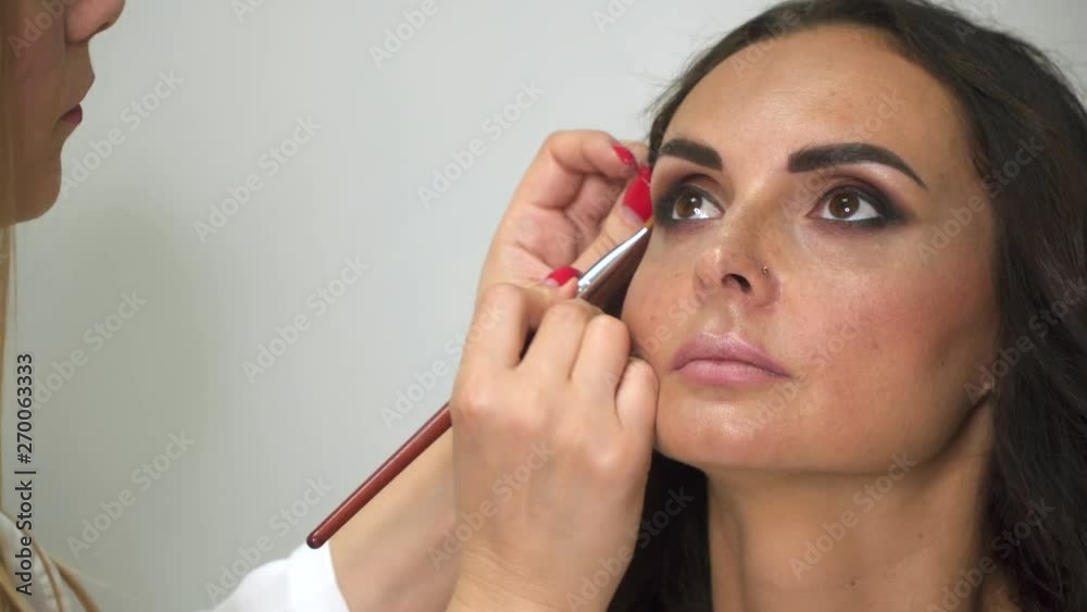 Makeup artist with brush puts shadows on the girl's face. Makeup artist with brush puts shadows on the girl's face.