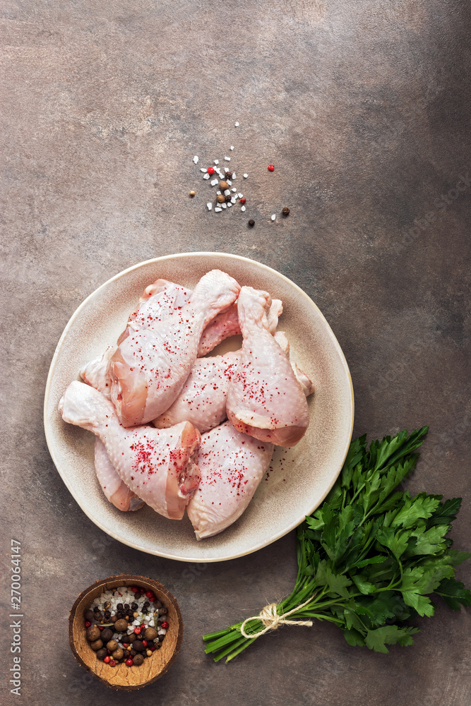 Raw chicken drumstick with spices and parsley on a dark rustic brown background. Top view, copy space.