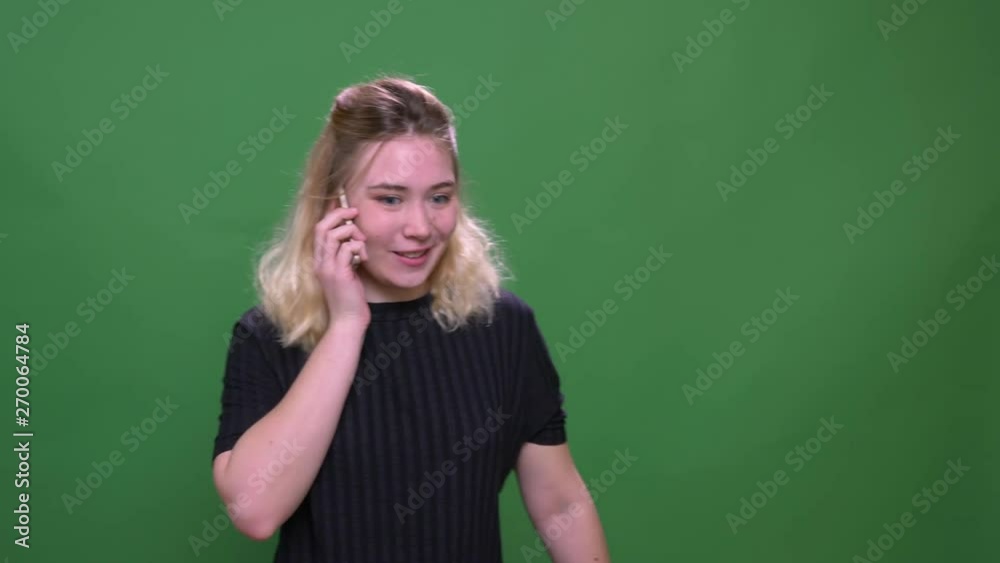 Closeup portrait of young pretty blonde caucasian female having a phone call with background isolated on green Closeup portrait of young pretty blonde caucasian female having a phone call with background isolated on green