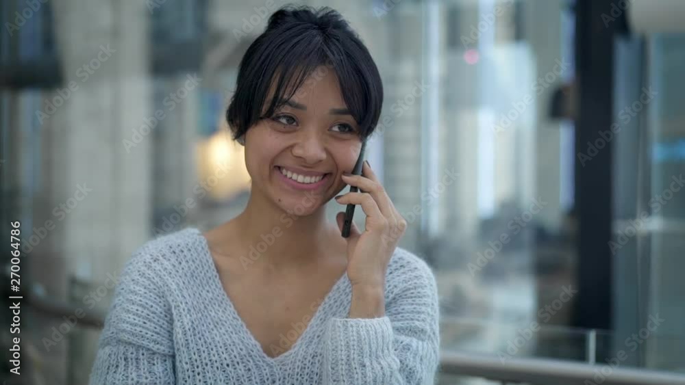 Pan shot slow motion of funny happy black hair asian female wearing grey sweatshirt talking on phone while walking. Business center