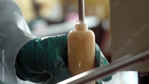 Laboratory assistants filling up bottle with body care lotion or shampoo in factory