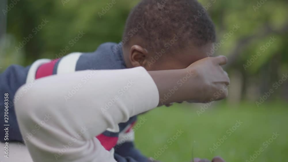 Close-up of little African American boy lying on top of his mother. The woman playing with a kid, pulling his nose. Mother and boy resting outdoors. Motherhood concept, family love Close-up of little African American boy lying on top of his mother. The woman playing with a kid, pulling his nose. Mother and boy resting outdoors. Motherhood concept, family love