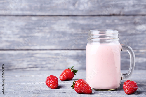 Smoothie in glass jar with strawberries on grey wooden table