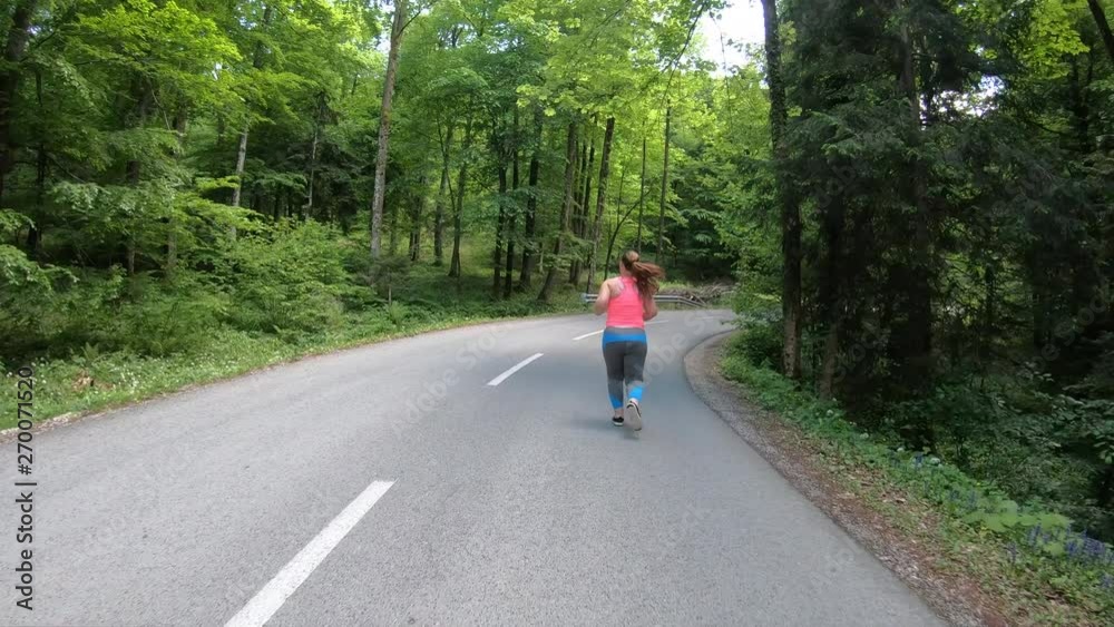 Wide forward tracking shot of a woman running on a road through the forest Wide forward tracking shot of a woman running on a road through the forest