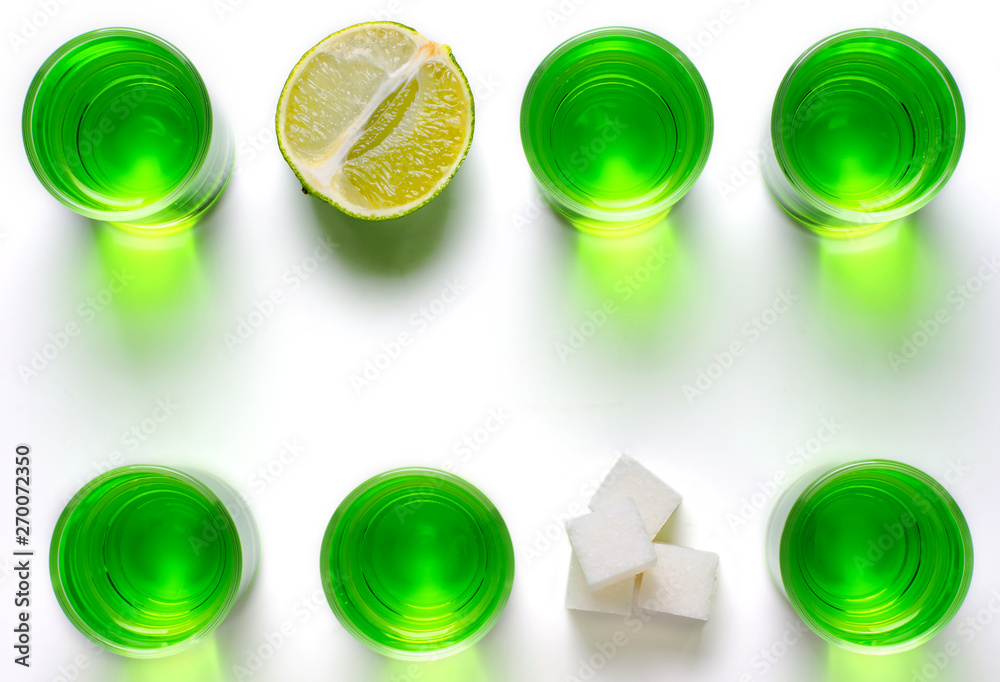 Absinthe green liquor in glasses. Alcoholic hallucinogenic beverage. White background. Pieces of lime and white sugar. Copy space. Flat lay Absinthe green liquor in glasses. Alcoholic hallucinogenic beverage. White background. Pieces of lime and white sugar. Copy space. Flat lay