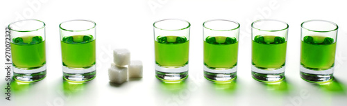 Absinthe green liquor in glasses. Alcoholic hallucinogenic beverage. White background. Pieces of white sugar.