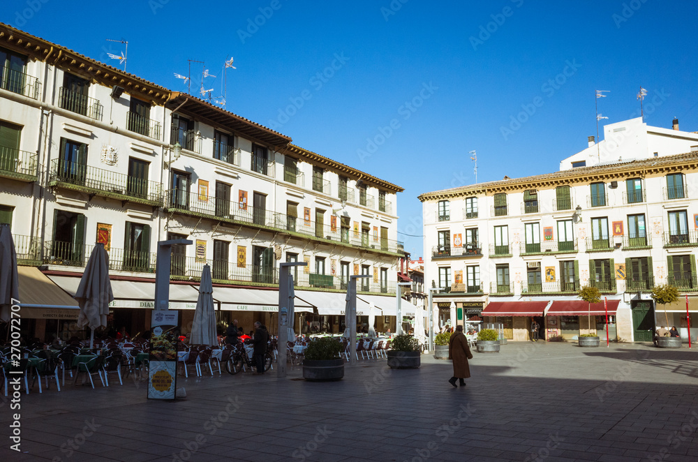 Tudela, Navarre, Spain - February, 13th, 2019 : Passersby at the 17th century Plaza Nueva or Plaza de los Fueros square, decorated with the coats of arms of the towns in La Ribera region of Navarre.