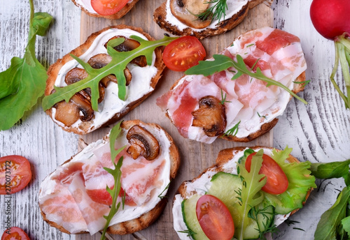 Bruschetta assortment with cream cheese, champignons, pancetta meat, vegetables and greenery photo