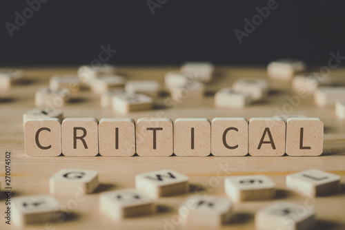 selective focus of word critical made of cubes surrounded by blocks with letters on wooden surface isolated on black