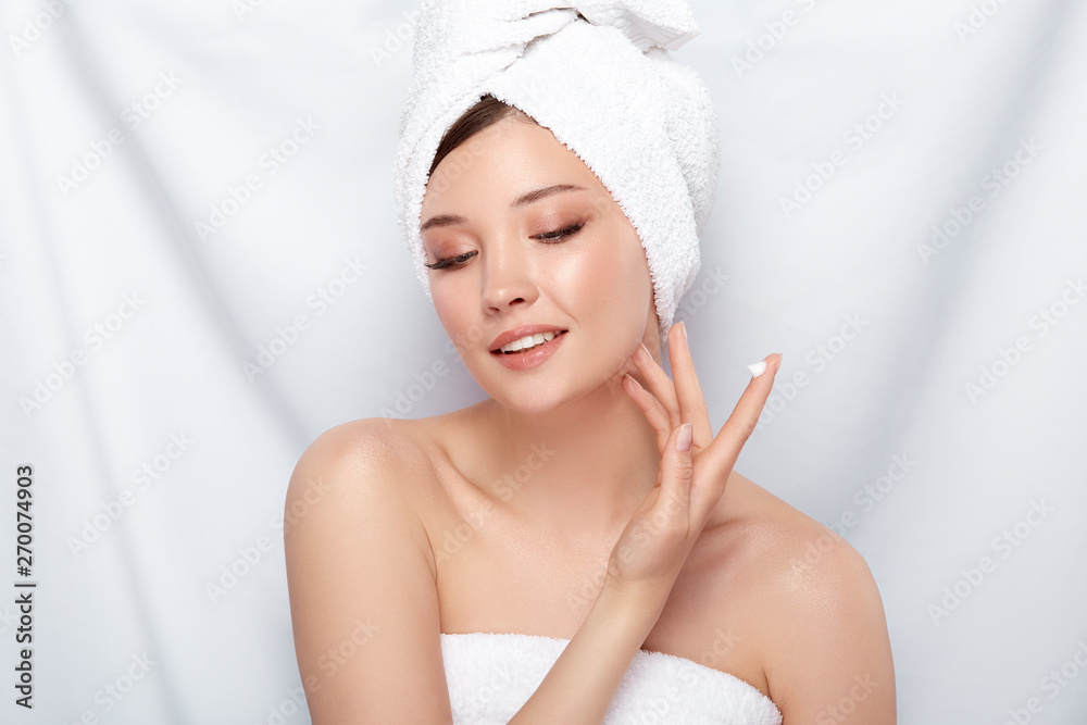 attractive woman in bath towel applying cream on her face isolated on white - obrazy, fototapety, plakaty 