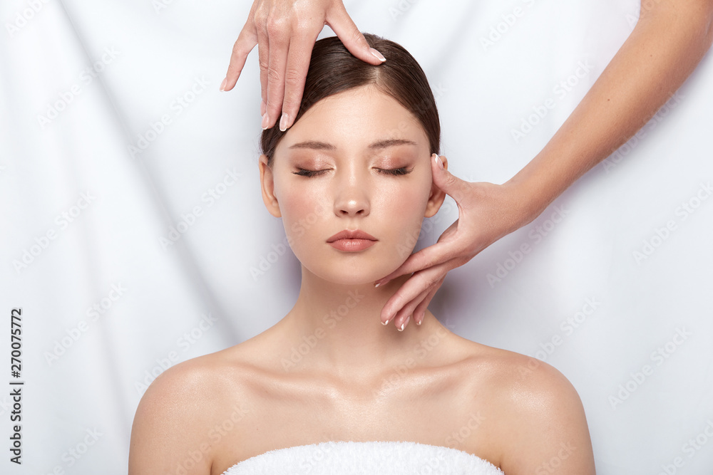 pretty girl lying down and receiving facial treatment, woman with naked shouders having massage for her face, body theraphy