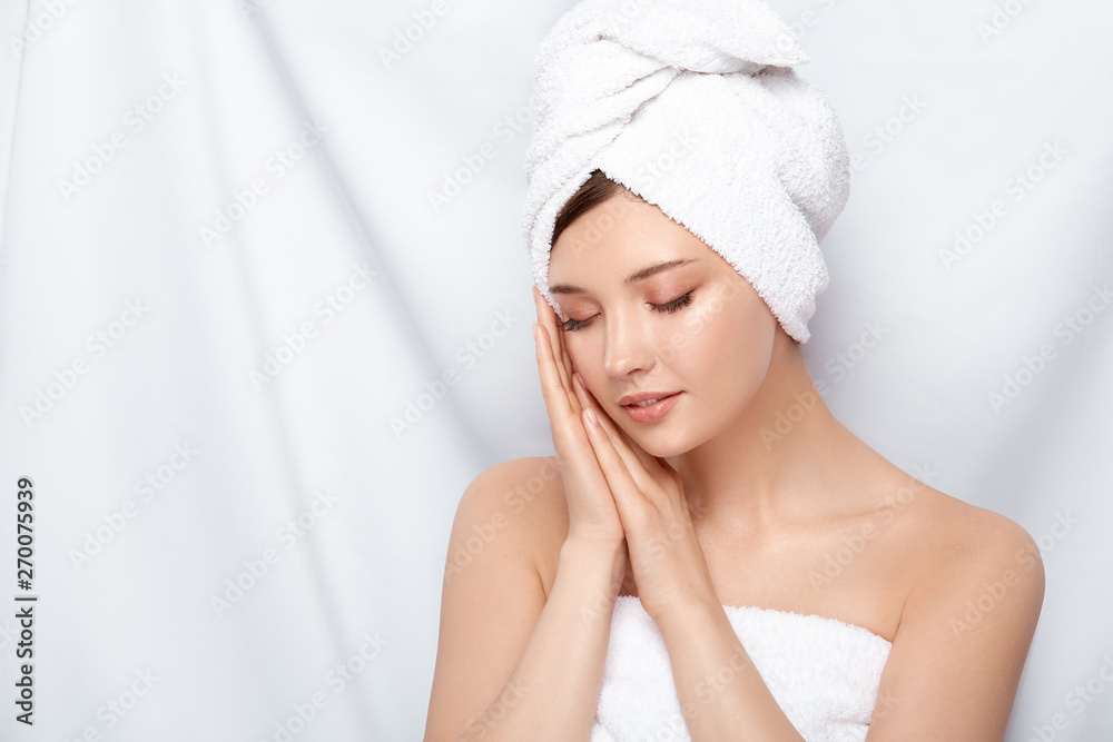 young and beautiful female in bath towel holding her hands near face with her eyes closed, pretty woman after treatment procedures - obrazy, fototapety, plakaty 