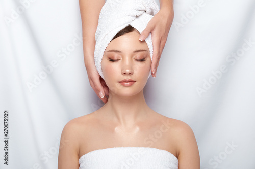 attractive woman lying down on spa theraphy in bath towel, customer of spa receiving facial treatment with beautician