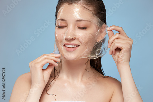 attractive girl with naked shouldes and wet hair taking off facial mask with eyes closed, copy space, pretty female purifying face