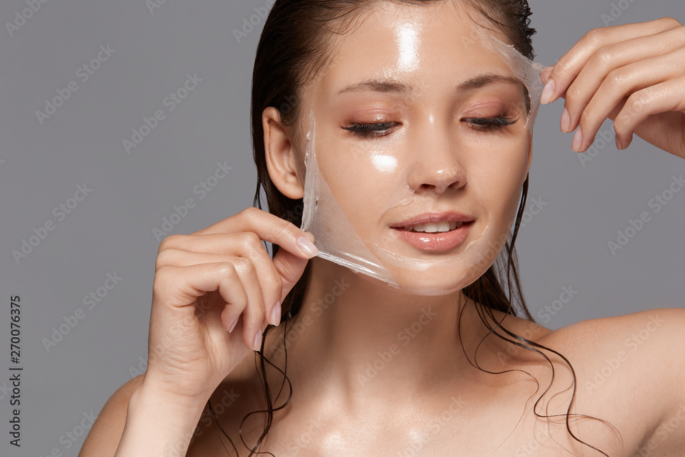 female with wet hair and naked shoulders removing trasparent peeling mask and looking down, copy space, woman facial treatment