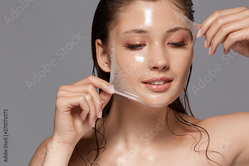 female with wet hair and naked shoulders removing trasparent peeling mask and looking down, copy space, woman facial treatment photo