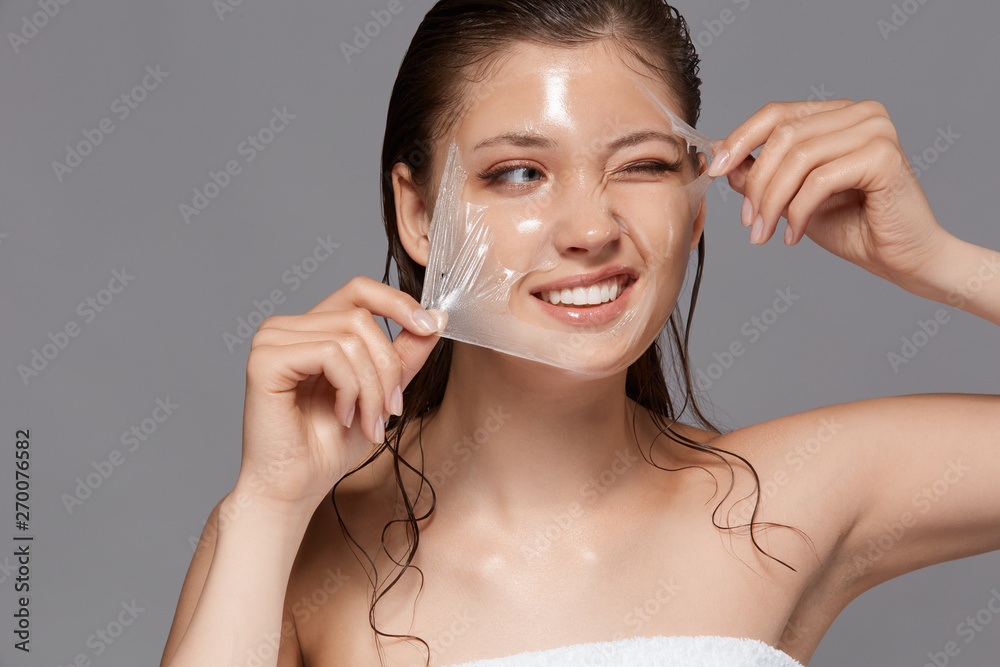 pretty girl removing purifiying facial mask with one eye closed and smile on face, skin treatment with beautiful lady