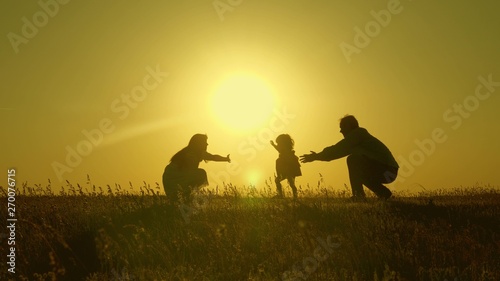 mother and Dad play with their daughter in sun. happy baby goes from dad to mom. young family in the field with a child 1 year. family happiness concept. beautiful sunshine  sunset.