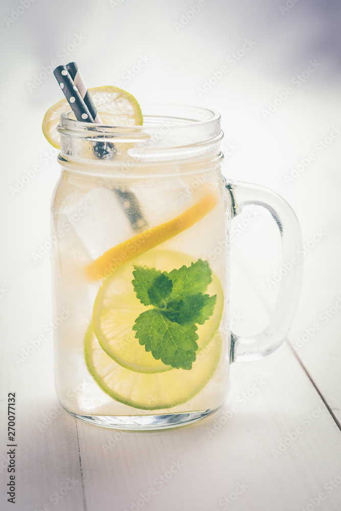 Lemonade Cocktail Mojito with Fresh Cold Ice, Lemon and Mint Leaves in Mason Jar on White Wooden Background. Bright Summer Concept. Lemonade Cocktail Mojito with Fresh Cold Ice, Lemon and Mint Leaves in Mason Jar on White Wooden Background. Bright Summer Concept.