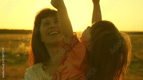 happy mother walks with her daughter in her arms in the rays of the sunset. Mom is talking with happy baby, baby is sitting on mother's arms at sunset of golden sun. Slow motion.