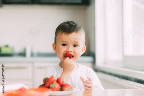 charming child in white t-shirt eating fresh homemade strawberries