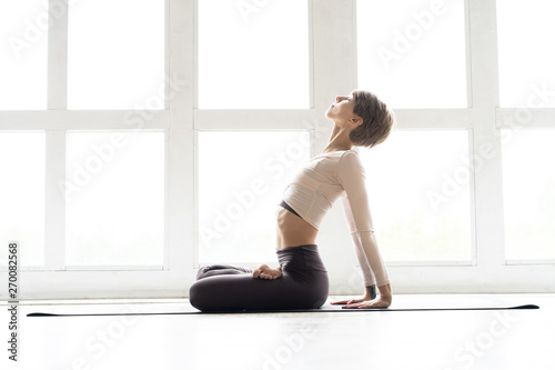 Young attractive smiling woman practicing yoga, sitting in Half Lotus exercise, Ardha Padmasana pose, working out, wearing sportswear.