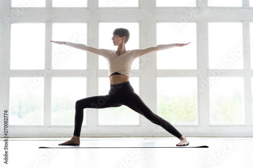 Young yogi woman practicing yoga, standing in Warrior two exercise, Virabhadrasana II pose, working out wearing sportswear. Weight loss concept.