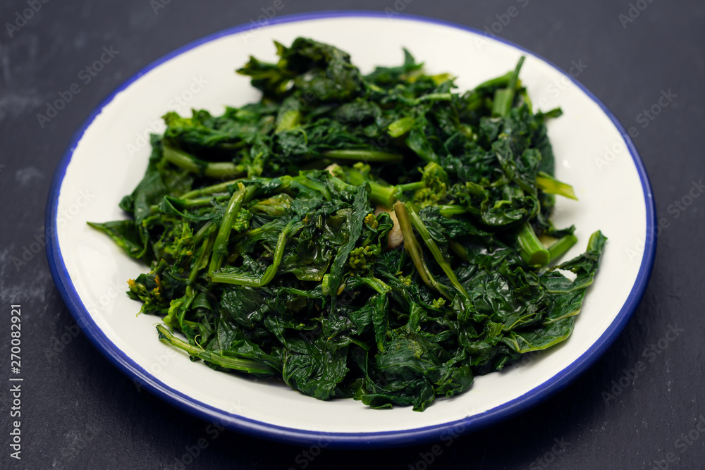 boiled greens with garlic on white plate on black ceramic background boiled greens with garlic on white plate on black ceramic background