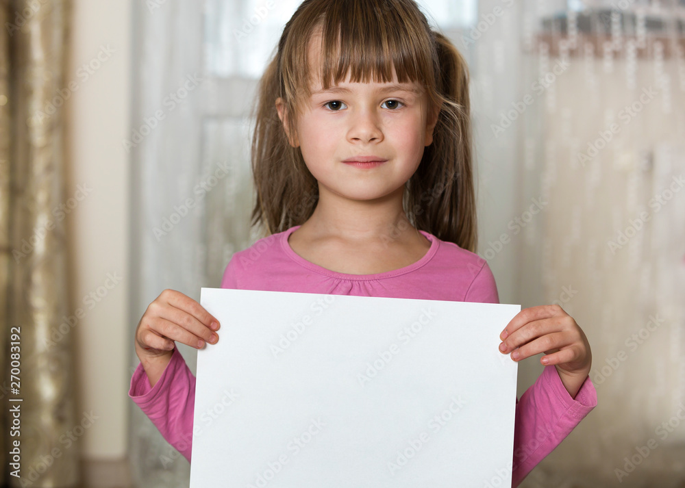 Happy smiling cute child girl holding white copy space sheet of drawing paper. Art education, creativity, advertisement concept. Happy smiling cute child girl holding white copy space sheet of drawing paper. Art education, creativity, advertisement concept.