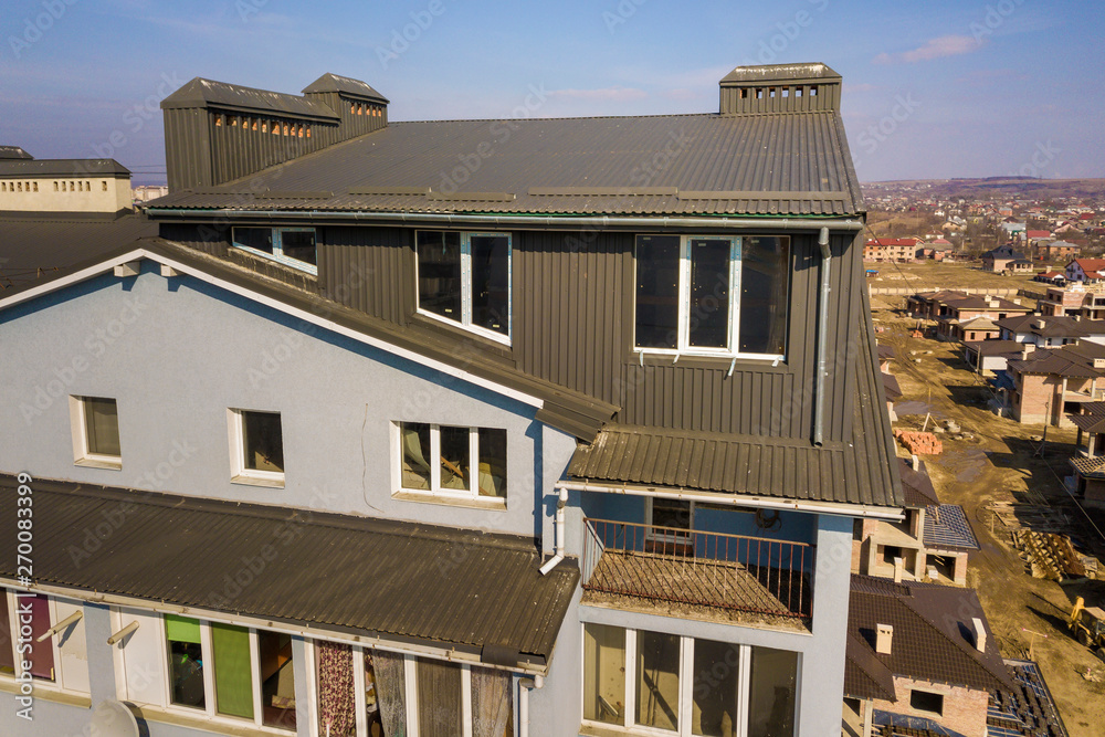 Aerial view of attic annex room exterior with plastic windows, roof and walls covered with brown metal decorative siding planks, new gutter system on top of apartment building.