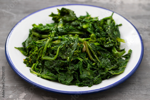 boiled greens with garlic on white plate on ceramic background