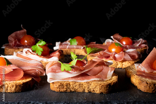 jamón serrano sobre pan tostado con tomate cherry y perejil, en clave oscura y presentado en plato de pizarra
