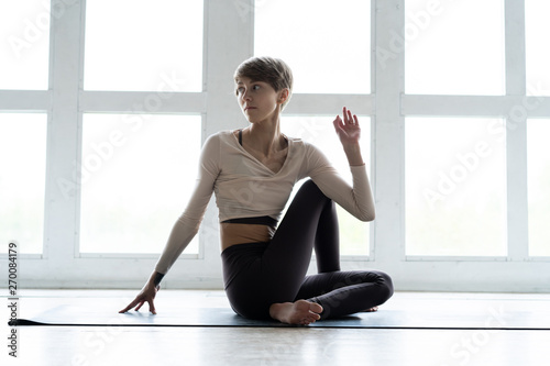 Young attractive woman practicing yoga, sitting in Ardha Matsyendrasana exercise, Half lord of the fishes pose, working out, wearing sportswear.